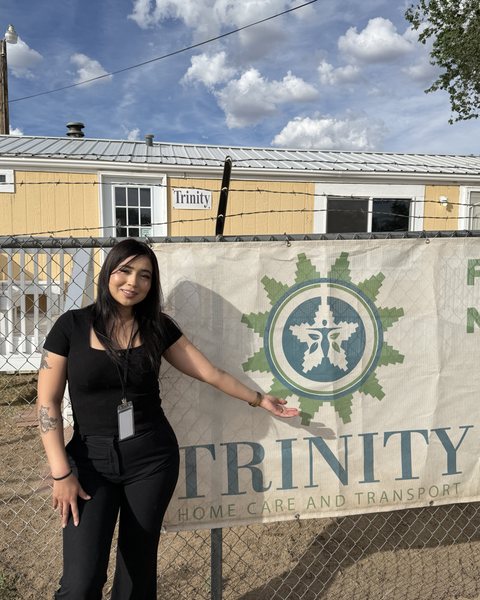 Akela Scott beside the Trinity banner on the fence outside the office on Highway 264 in Window Rock