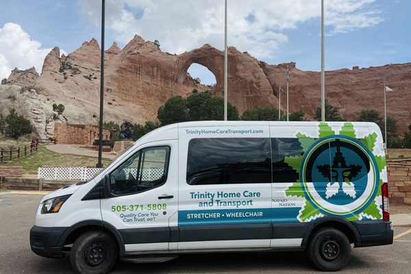 A Trinity Home Care and Transport van parked in front of the Window Rock, with the Navajo Code Talkers memorial behind it
